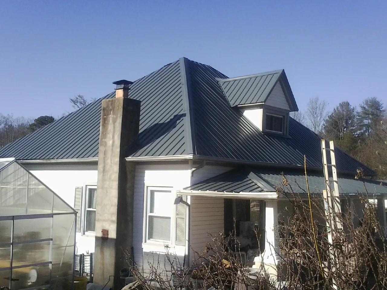 Dark blue standing seam metal roof on a white farmhouse with dormer — Slate & Tile Roof Repair by Roofing Brothers in Three Lakes