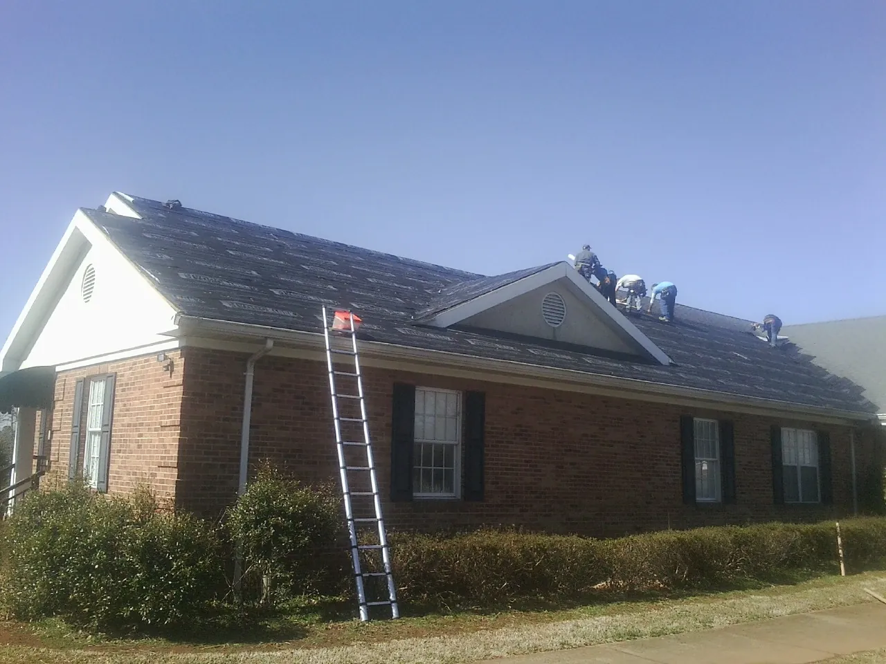 Crew tearing shingles off a brick ranch roof with a ladder set — Emergency Roof Repair work by our crew in Three Lakes