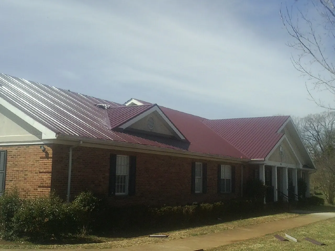 Red metal roof with gabled entries on a long brick building, from a Hail Damage Roof Repair job in Three Lakes