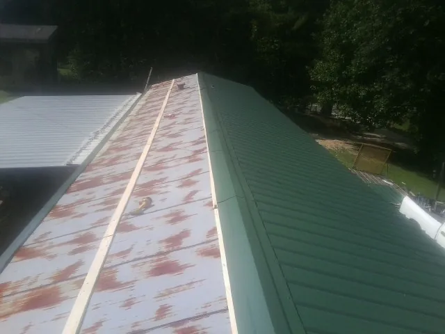 Old rusted panels beside newly installed green metal roofing — Wind Damage Roof Repair by Roofing Brothers in Three Lakes