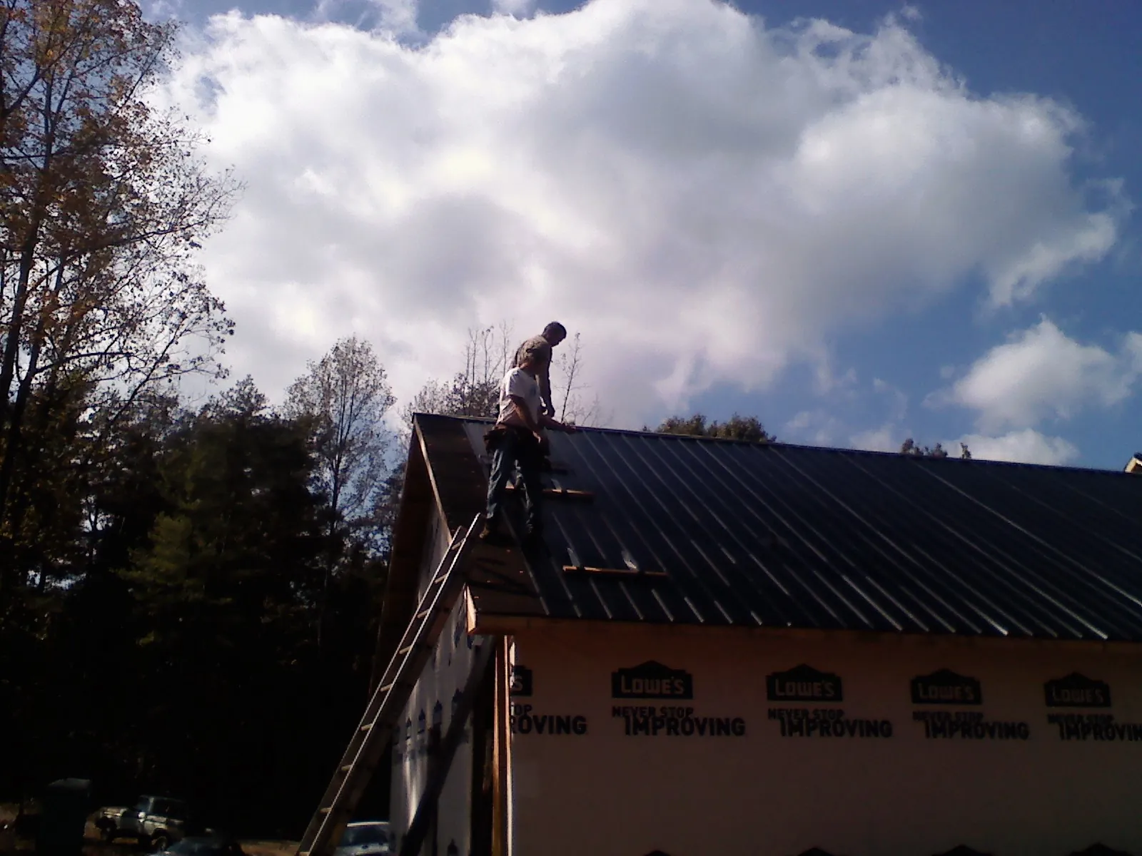 Roofer fastening dark metal panels high against a cloudy sky, from a Roof Inspection job in Three Lakes